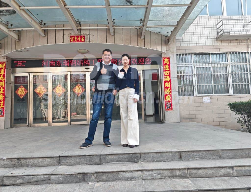 Two professionals standing in front of a modern building entrance, smiling and giving thumbs up.