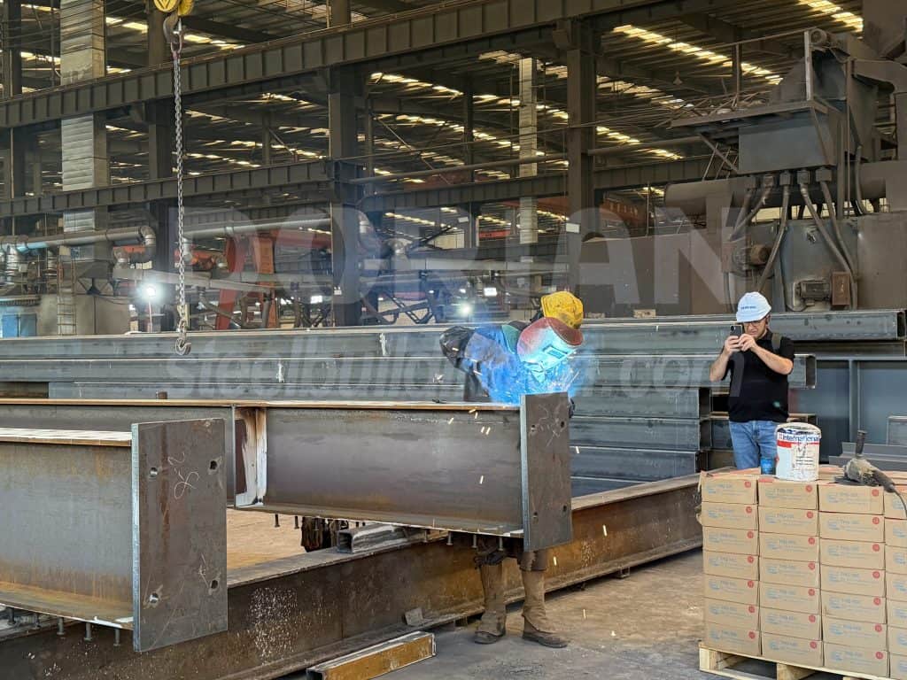 Workers welding steel beams in a factory for steel building construction.