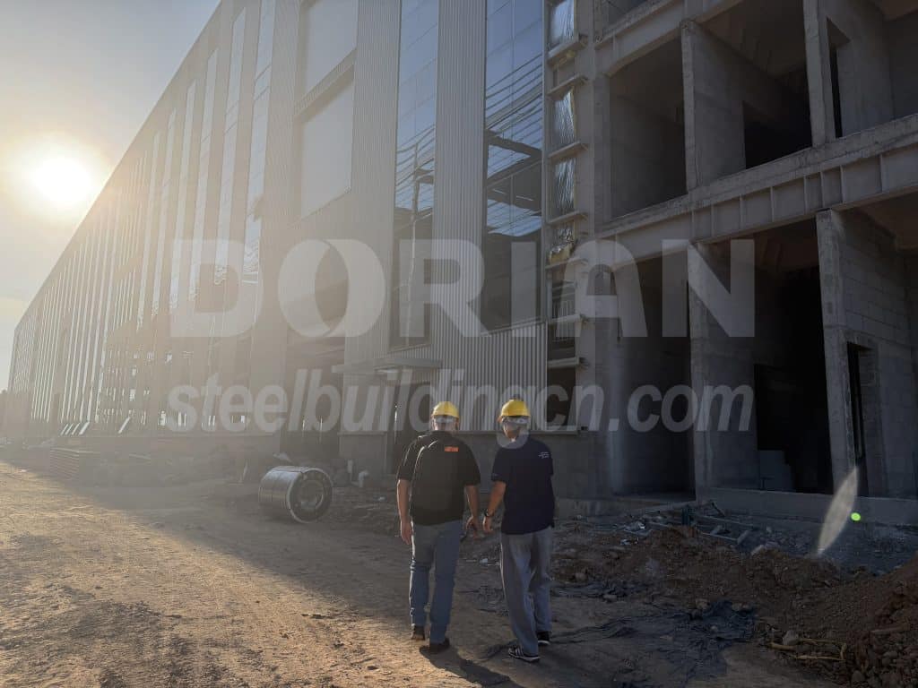 Steel building under construction with workers inspecting the site.