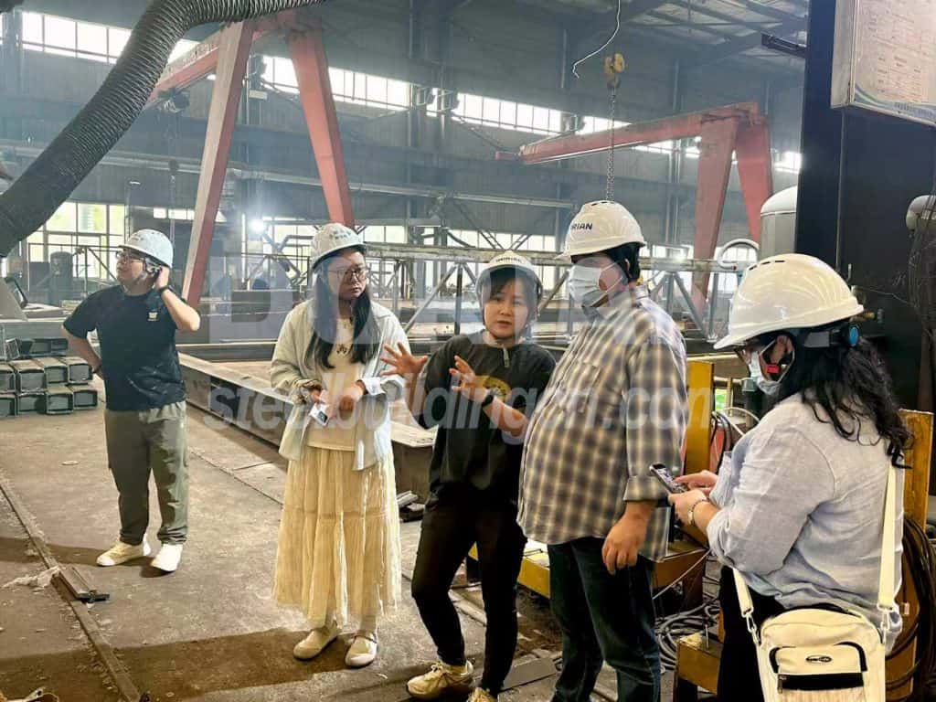 Group of engineers and workers inspecting steel building components in factory.